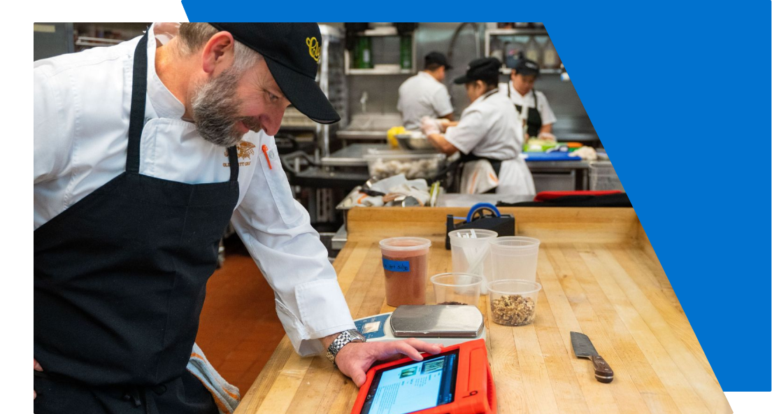 man with black apron looking at a tablet